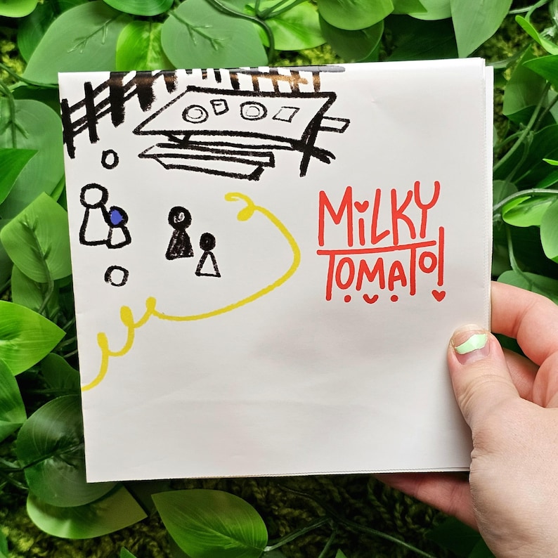 May include: A white card with black and yellow drawings of people and a table. The text "MILKY TOMATO!" is written in red.