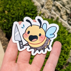 K&ouml;nnte beinhalten: Ein gelber und schwarzer Bienensticker mit einem blauen und wei&szlig;en Fl&uuml;gel, der ein silbernes Messer h&auml;lt. Die Biene hat einen fr&ouml;hlichen Ausdruck mit einem breiten L&auml;cheln und roten Wangen.