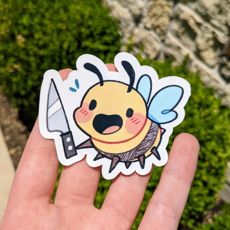 K&ouml;nnte beinhalten: Ein gelber und schwarzer Bienensticker mit einem blauen und wei&szlig;en Fl&uuml;gel, der ein silbernes Messer h&auml;lt. Die Biene hat einen fr&ouml;hlichen Ausdruck mit einem breiten L&auml;cheln und roten Wangen.