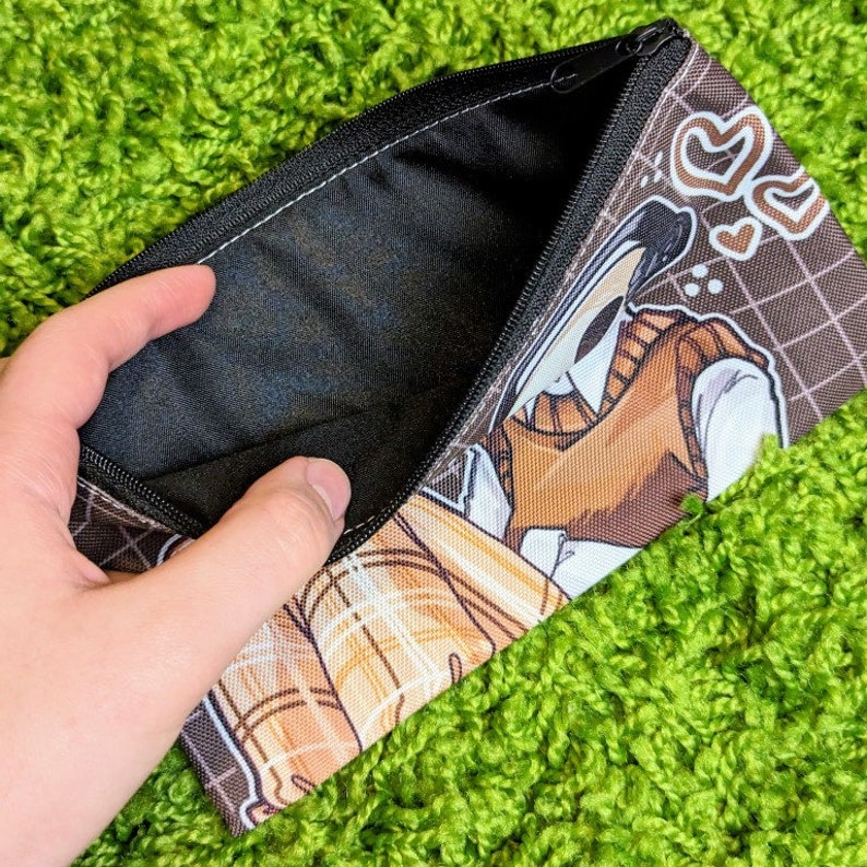 May include: A brown and black zippered pencil case with a white and brown illustration of a person wearing a brown sweater vest and a white shirt. The illustration is on a brown and white grid pattern background. The zipper is open and the inside of the case is black.