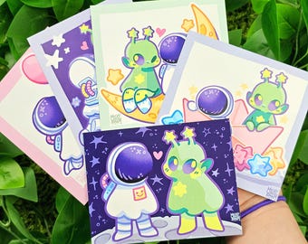 Puede incluir: Conjunto de cinco tarjetas ilustradas con personajes de dibujos animados lindos en el espacio. Los personajes incluyen astronautas y extraterrestres. Las tarjetas están impresas en cartulina blanca con un fondo rosa claro, azul claro y verde claro. Las tarjetas tienen un diseño caprichoso y colorido.