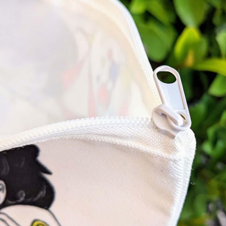 May include: White zippered pouch with a white zipper pull. The pouch has a colorful design on the front.