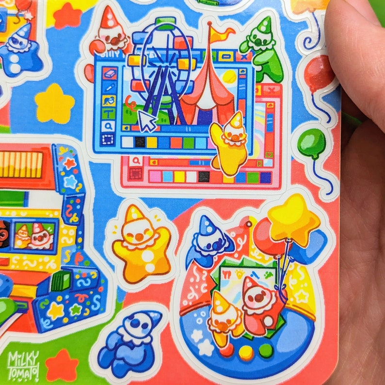 May include: A set of colorful stickers featuring cartoon clowns, a Ferris wheel, a star, a computer screen, and a blue and white game console. The stickers are on a pink and blue background.