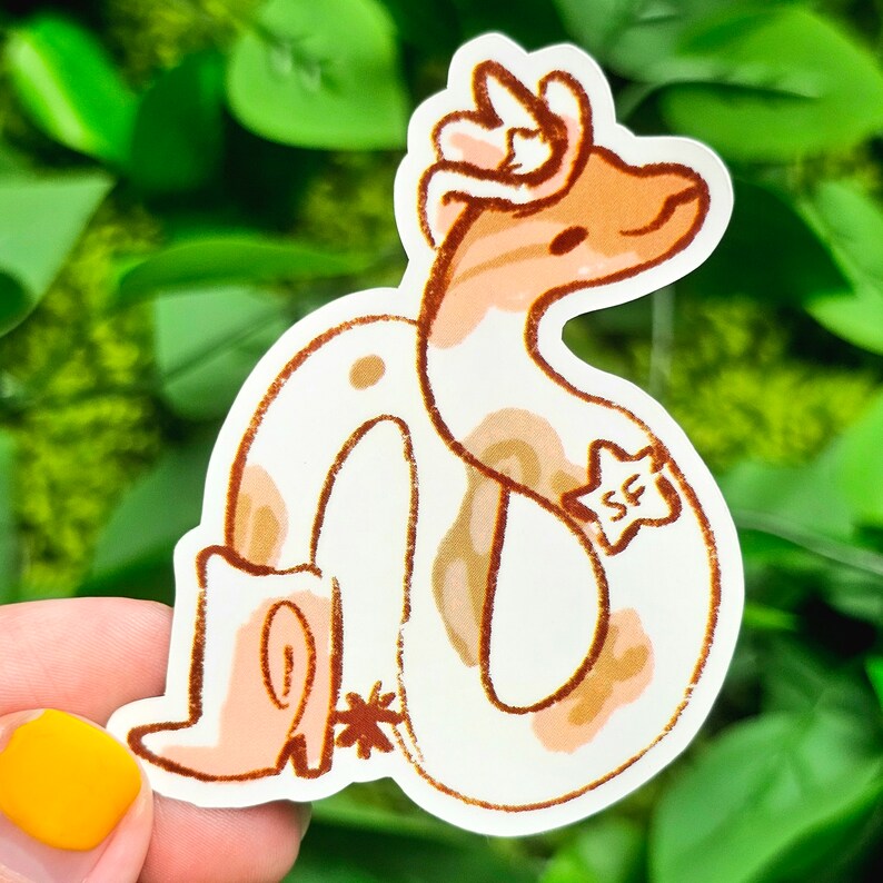 Puede incluir: Una pegatina de serpiente blanca y marr&oacute;n con una corona rosa y marr&oacute;n en la cabeza. La serpiente est&aacute; enroscada y tiene una estrella con las letras "SF" en un lado.