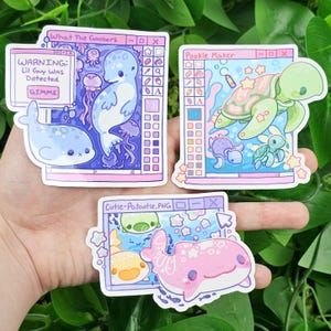 May include: Three digital art stickers featuring cute sea creatures. The first sticker shows a blue seal with a warning message that reads "WARNING: Lil Guy Was Detected GIMME". The second sticker shows a green sea turtle with a pink, blue, and white background. The third sticker shows a pink and white spotted fish with a blue, yellow, and white background.