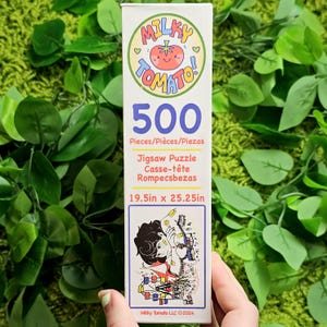 May include: A 500-piece jigsaw puzzle box featuring a colourful illustration of a person standing in front of a Ferris wheel. The box is white with a red tomato logo and the text "Milky Tomato!" in a pink and blue font. The puzzle measures 49.5 cm by 64.1 cm.