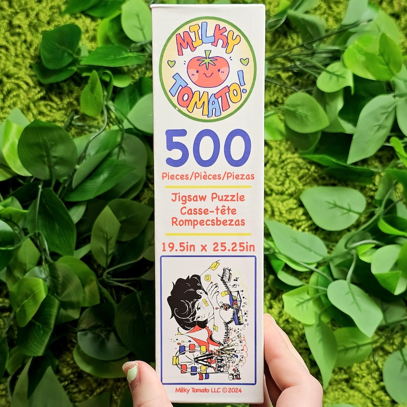May include: A 500-piece jigsaw puzzle box featuring a colourful illustration of a person standing in front of a Ferris wheel. The box is white with a red tomato logo and the text "Milky Tomato!" in a pink and blue font. The puzzle measures 49.5 cm by 64.1 cm.