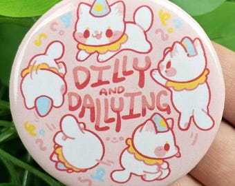 May include: A round, pink button featuring cartoon white cats with party hats and yellow collars. The text "DILLY AND DALLYING" is in the center. The button has a playful, whimsical design.