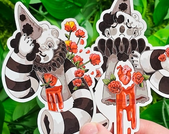 May include: Two stickers featuring a clown design with black and white striped arms and legs, a ruffled collar, and a pointed hat. One clown has red roses and the other has a heart and red blood dripping down.
