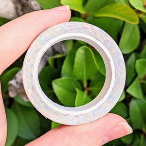 May include: A roll of colourful washi tape with a white core. The tape has a speckled pattern with shades of pink, blue, yellow, and green.
