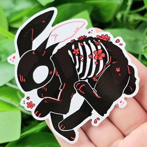 May include: Black and white rabbit sticker with red flowers on its body. The rabbit has a skeletal appearance with a white background.