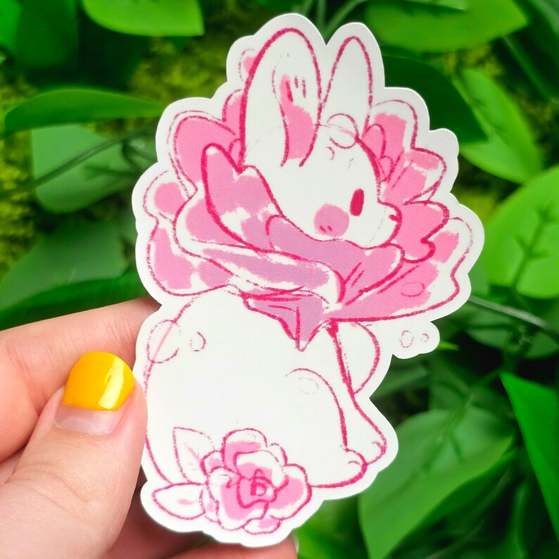 Puede incluir: Un conejito blanco con orejas rosas y una flor rosa alrededor del cuello. El conejito est&aacute; sentado en una flor rosa con hojas verdes.