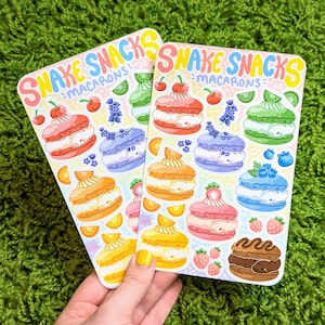 May include: Two sheets of stickers featuring colorful macarons with snakes inside. The stickers are labeled "Snake Snacks - Macarons".