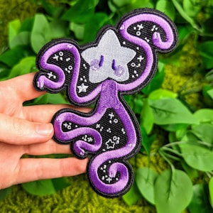 May include: Purple and white embroidered patch of a cartoon star with a face and a swirling body, with a black background and white stars.