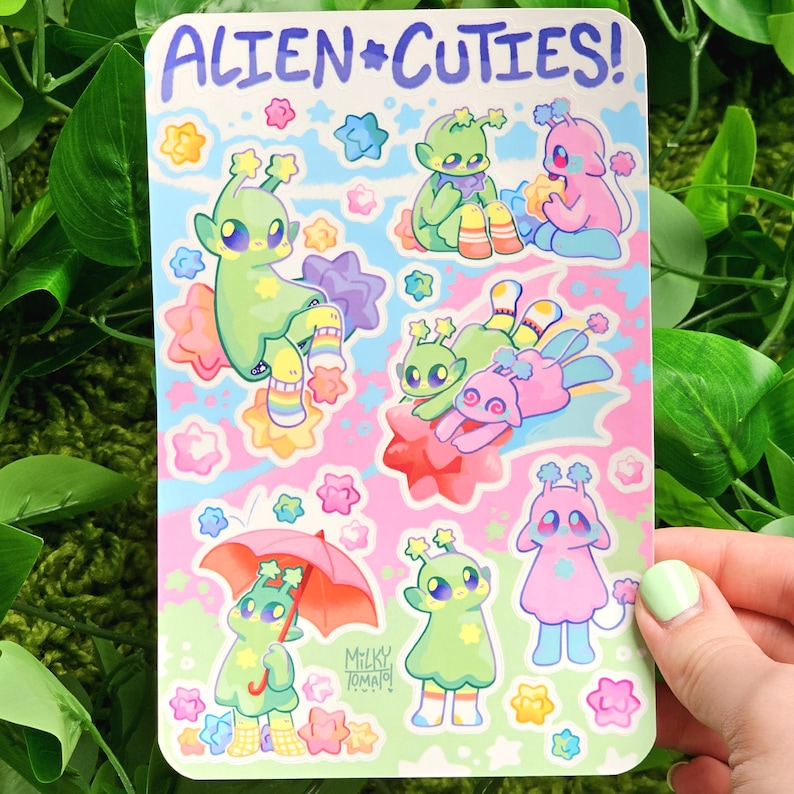 May include: A sheet of stickers featuring cute alien characters with stars and other space-themed designs. The stickers are on a pink background with a light blue and green gradient. The text "Alien*Cuties!" is at the top of the sheet.