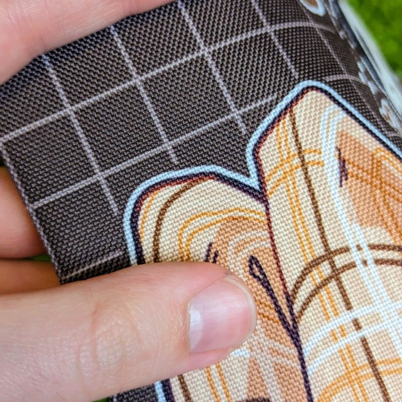 May include: Close-up of a brown fabric with a grid pattern. The fabric has a colorful design printed on it, featuring a geometric pattern with curved lines and a light brown color.