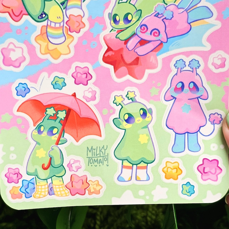 May include: A set of colorful stickers featuring cartoon aliens with stars and flowers. The stickers are on a pink background with green accents. The text "Milky Tomato!" is visible in the bottom right corner.
