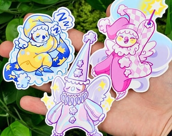 May include: Three whimsical stickers featuring cartoon characters. One sticker depicts a sleeping figure in a yellow and blue outfit. Another shows a pink jester with a magic wand. The third sticker is a light purple jester with wings and stars.