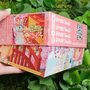 May include: A pink and white jigsaw puzzle box with a Japanese-inspired illustration of a bridge, cherry blossoms, and two figures in traditional clothing. The box is 19.5 inches by 25.25 inches and features the text "Milky Tomato LLC &copy;2024" and social media handles for @milky.tomato.