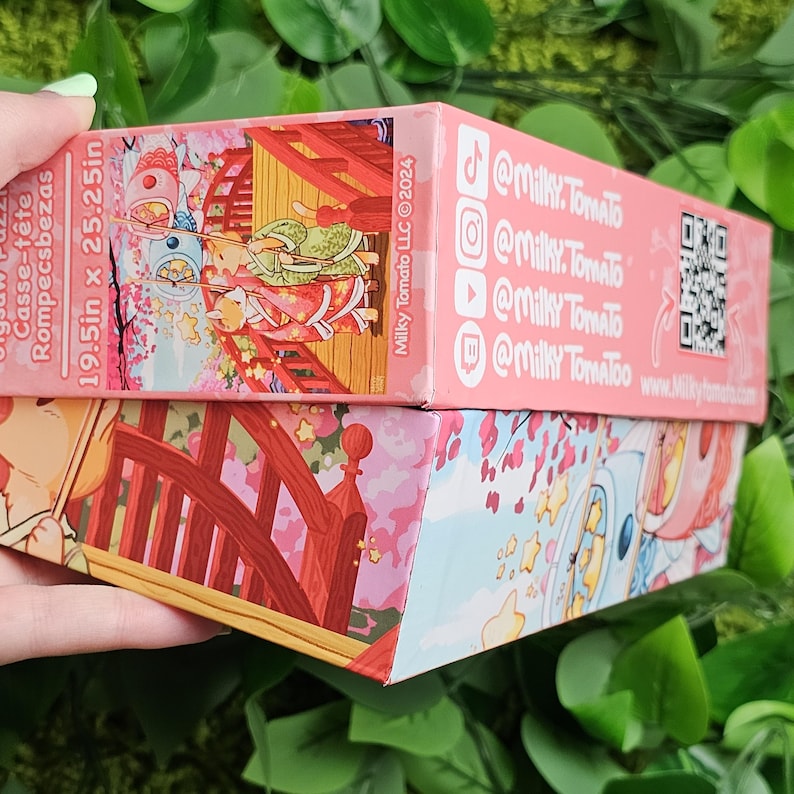 May include: A pink and white jigsaw puzzle box with a Japanese-inspired illustration of a bridge, cherry blossoms, and two figures in traditional clothing. The box is 19.5 inches by 25.25 inches and features the text "Milky Tomato LLC &copy;2024" and social media handles for @milky.tomato.