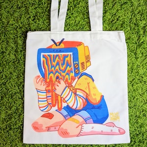 May include: A white tote bag with a colorful illustration of a person with a television for a head. The television is melting and dripping. The text "Milky Tomato" is printed on the bag.
