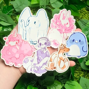 Puede incluir: Un conjunto de nueve pegatinas coloridas con varios personajes de dibujos animados. Las pegatinas incluyen una oveja rosa esponjosa, un ping&uuml;ino azul, un esqueleto morado, una serpiente marr&oacute;n, un conejito blanco con una flor rosa y un p&aacute;jaro blanco con alas azules.