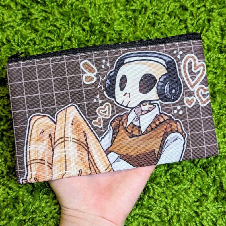 May include: A brown and black zippered pouch with a cartoon skeleton wearing headphones and a brown sweater vest. The skeleton is sitting with its legs crossed and wearing plaid pants. The background is a brown grid pattern with hearts and other doodles.