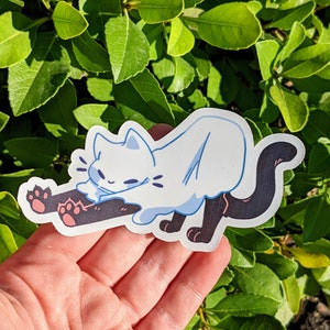 K&ouml;nnte beinhalten: Eine wei&szlig;e Katze mit schwarzen Beinen streckt sich im Cartoon-Stil. Die Katze tr&auml;gt ein wei&szlig;es Geisterkost&uuml;m mit einem schwarzen Schwanz.