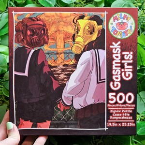 May include: A 500-piece jigsaw puzzle featuring two girls wearing gas masks in front of a fiery explosion. The puzzle box has a pink and white logo with the text "Milky Tomato! Gasmask Girls!" and the dimensions "19.5in x 25.25in".