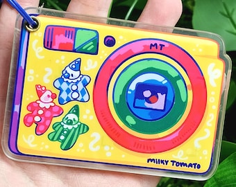 May include: A yellow and clear plastic camera charm with a rainbow lens and three cartoon clowns. The camera has the text "MT" and "MIKEY TOMATO" on it.