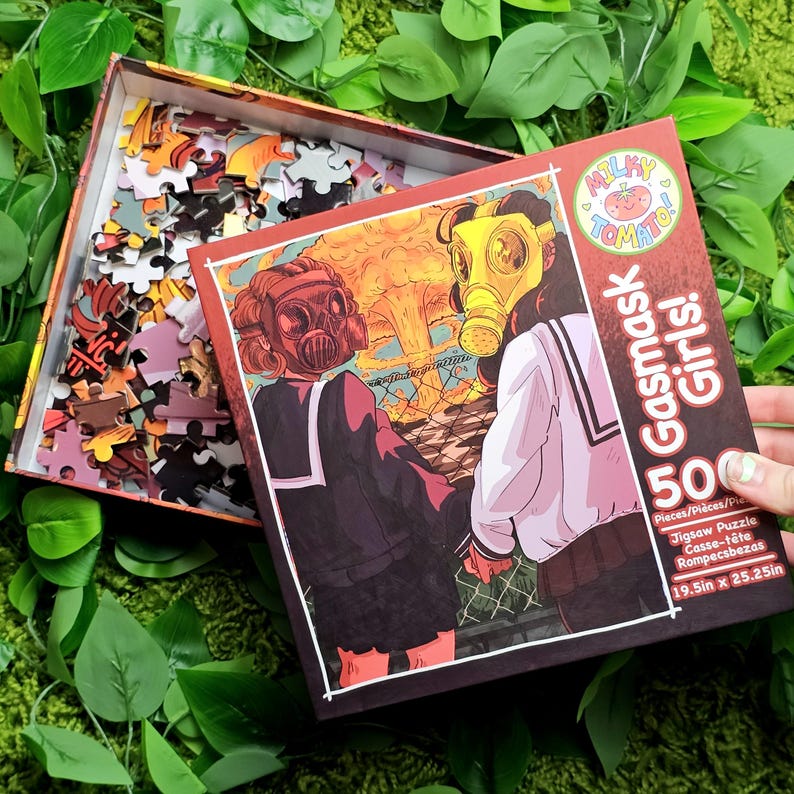 May include: A 500-piece jigsaw puzzle box featuring two girls wearing gas masks. The girls are standing in front of a large explosion. The box is red and white with the text "Milky Tomato Gasmask Girls!" and "19.5in x 25.25in".