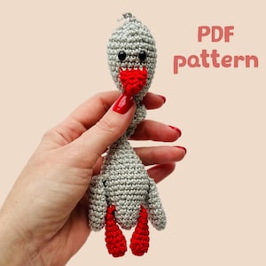 May include: Crochet pattern for a gray goose with red beak and legs. The pattern is available as a PDF download.