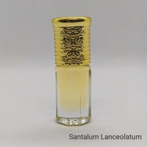 May include: A small, clear glass bottle filled with a pale yellow liquid. The bottle has a decorative gold-colored cap with ornate detailing. The text "Santalum Lanceolatum" is printed at the bottom of the image.