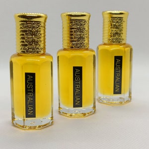 May include: Three perfume bottles with gold-colored caps and clear glass bodies. The bottles are filled with a yellow liquid. Each bottle has a black label that reads "AUSTRALIAN".