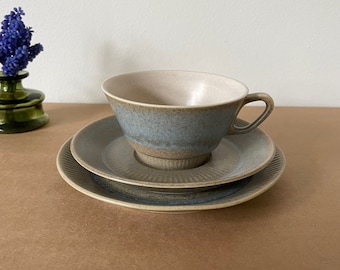 May include: A set of three ceramic teacups in shades of blue and brown. The cup and saucer have a textured, rippled design.