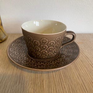 以下が含まれることがあります： 花柄の茶碗と受け皿のセット。茶碗と受け皿はどちらも、小さな浮き彫りの花が繰り返し描かれた模様で飾られています。