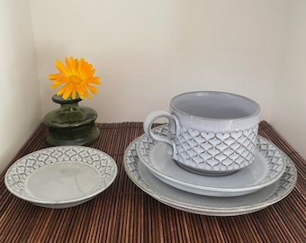 May include: A gray ceramic teacup and saucer set with a delicate heart pattern. The cup has a handle and the saucer is slightly larger than the cup. The set is on a brown bamboo mat.