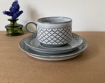May include: A gray ceramic teacup and saucer set with a geometric pattern. The cup has a handle and the saucer has a raised edge.