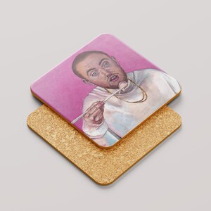 May include: Square coaster featuring a watercolor portrait of a man with a gold chain, holding a marshmallow on a stick. The coaster has a pink background and sits atop a cork coaster.