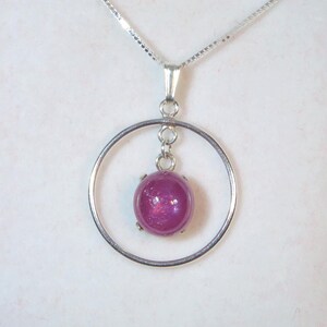 May include: A silver necklace with a pink gemstone pendant in a circle setting. The necklace is displayed in a red velvet box.