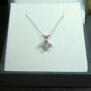 May include: A silver necklace with a small pendant featuring a square design with four clear and pink gemstones.