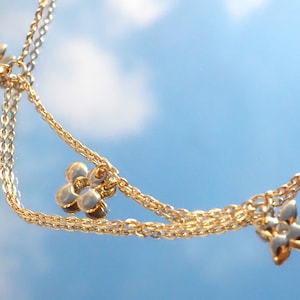 May include: A gold chain necklace with three flower-shaped charms. The necklace is layered and has a delicate design.