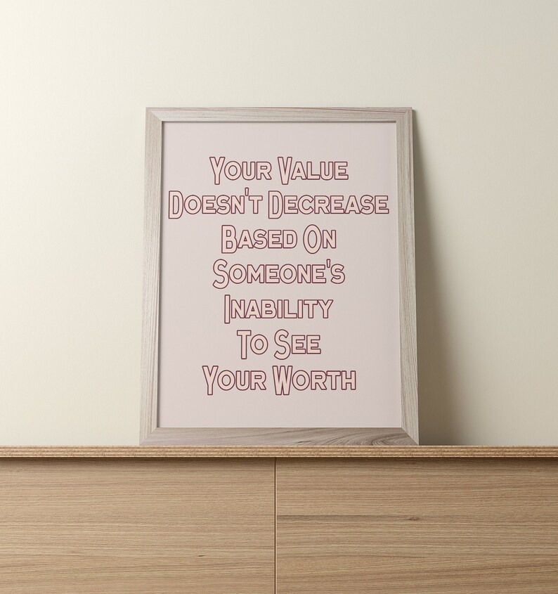 May include: A framed print with a pink background and white text that reads "Your value doesn't decrease based on someone's inability to see your worth". The frame is light wood.