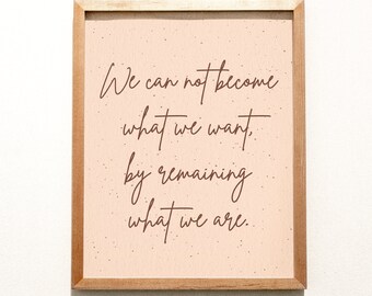Könnte beinhalten: Ein gerahmter Druck mit beigefarbenem Hintergrund und braunem Text, der "We can not become what we want, by remaining what we are." lautet.