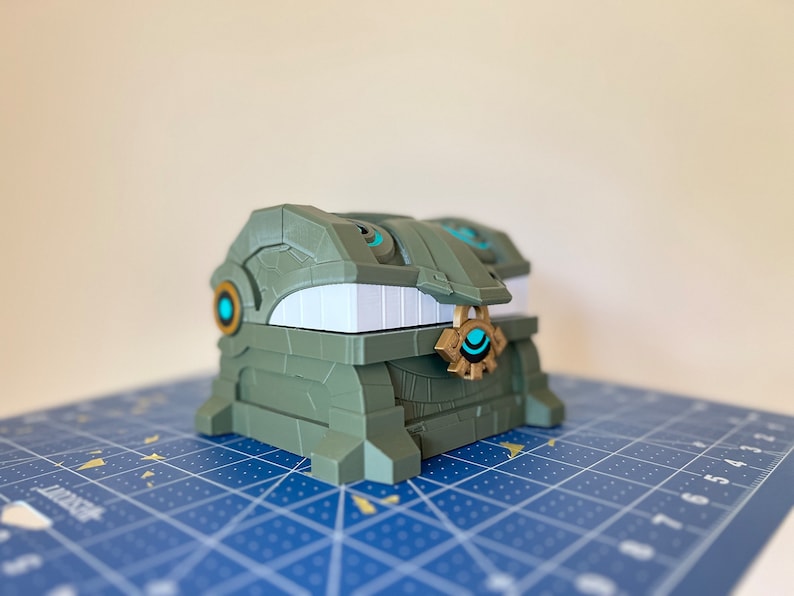 May include: A green and gold treasure chest with a blue eye design. The chest is made of plastic and has a detailed design.