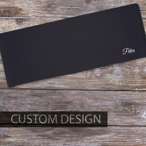 May include: A black personalized mouse pad with the name "Peter" embroidered in white on a wooden surface.