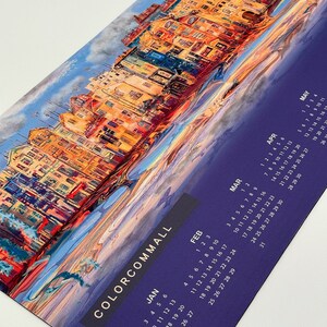 K&ouml;nnte beinhalten: Ein farbenfroher Kalender mit einem Gem&auml;lde einer Stadtlandschaft. Der Kalender ist lila mit goldenen Buchstaben und umfasst die Monate Januar bis Mai.