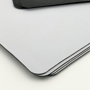 K&ouml;nnte beinhalten: Ein Stapel wei&szlig;er Mauspads mit schwarzen Kanten. Die Mauspads sind aus einem glatten, weichen Material gefertigt.