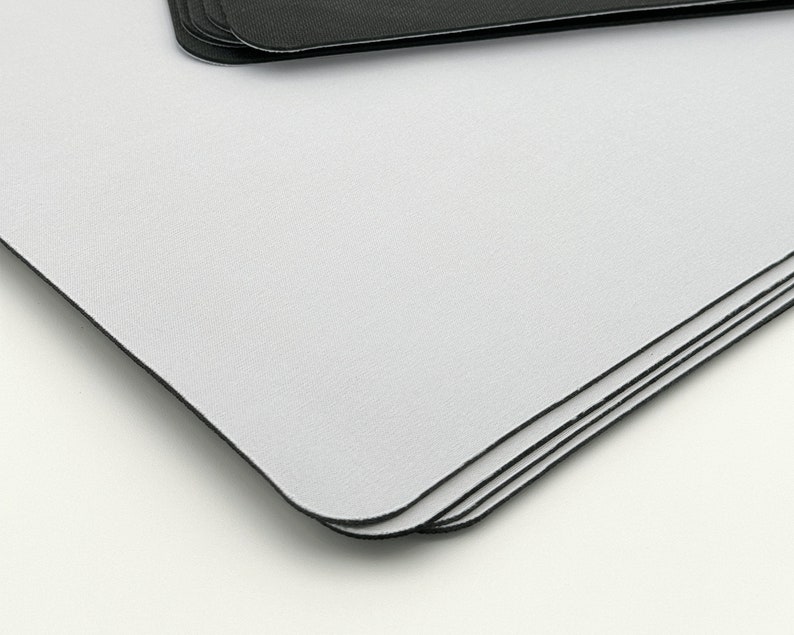 K&ouml;nnte beinhalten: Ein Stapel wei&szlig;er Mauspads mit schwarzen Kanten. Die Mauspads sind aus einem glatten, weichen Material gefertigt.