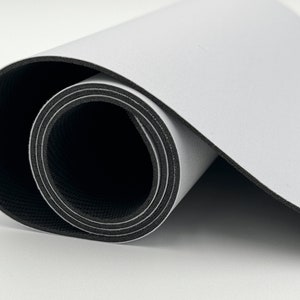 K&ouml;nnte beinhalten: Eine wei&szlig;e und schwarze zusammengerollte Yogamatte. Die Matte ist mit der schwarzen Seite nach au&szlig;en und der wei&szlig;en Seite nach innen zusammengerollt.
